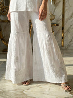 White embroidered pants worn by a person in an elegant interior setting.