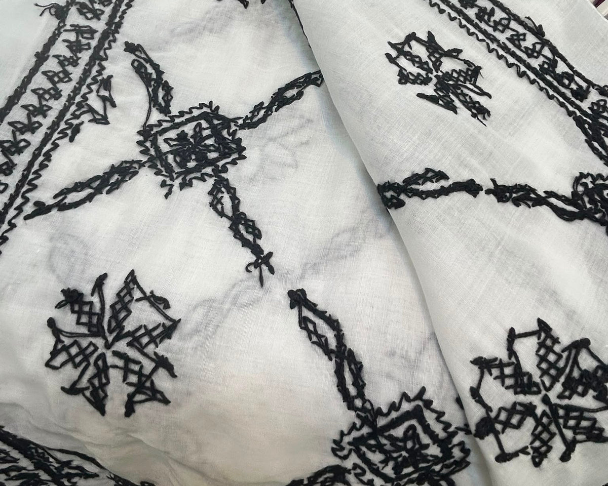 White fabric with black embroidered patterns on a textured surface