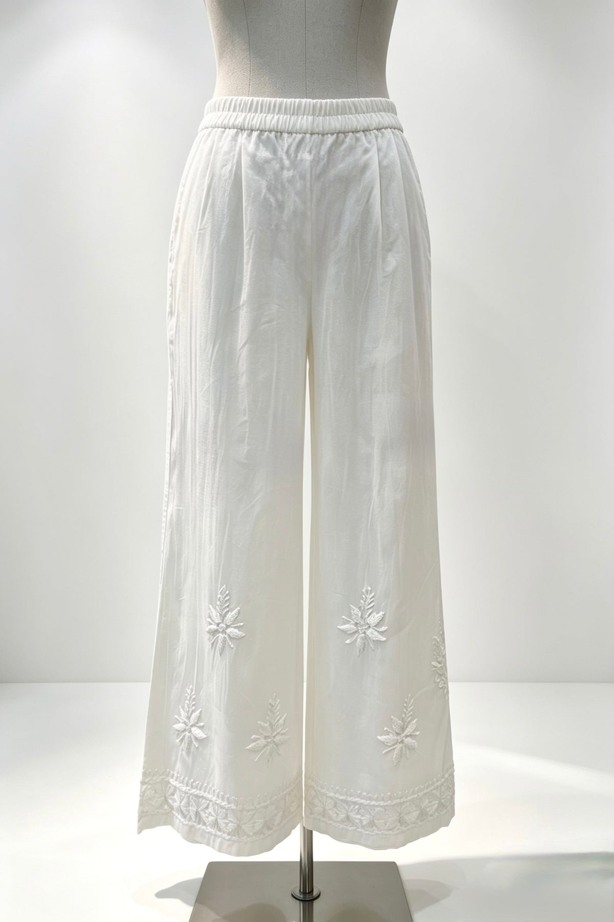 White pants with floral embroidery on a mannequin against a white background