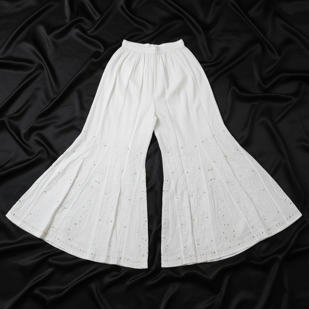 White wide-leg flared pants with a subtle eyelet pattern, laid flat on a light wood floor.