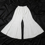 White wide-leg flared pants with a subtle eyelet pattern, laid flat on a light wood floor.