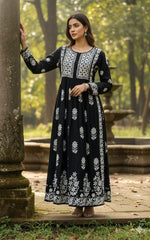 Woman in a black and white chikankari embroidered dress standing outdoors in a garden.