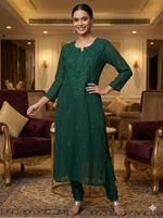 Woman in a green dress standing in an elegant room with purple sofas and gold accents.