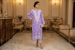 Woman in a lilac embroidered dress standing in an elegant room with classical décor.