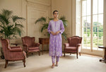 Woman in a lilac outfit standing in an elegant room with classical décor.