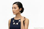 Woman wearing a navy dress with a gold and pearl necklace on a white background