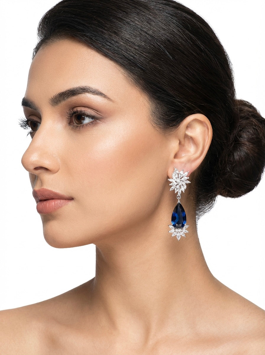Woman wearing a pair of earrings with a blue gemstone on a white background