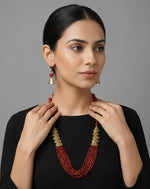 Woman wearing a red beaded necklace and earrings against a gray background