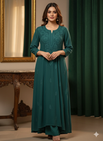 Woman wearing a teal dress with intricate patterns in a room with a mirror and green curtains.