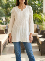 Woman wearing a white embroidered top and blue jeans in an outdoor setting
