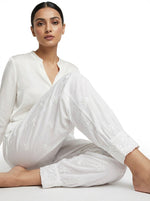 Woman wearing a white saree with intricate designs on a plain background