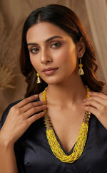 Woman wearing a yellow beaded necklace and earrings against a neutral background