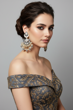 Woman wearing an off-shoulder dress with intricate patterns and large earrings against a gray background