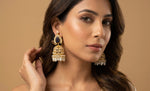 Woman wearing gold earrings with a beige background