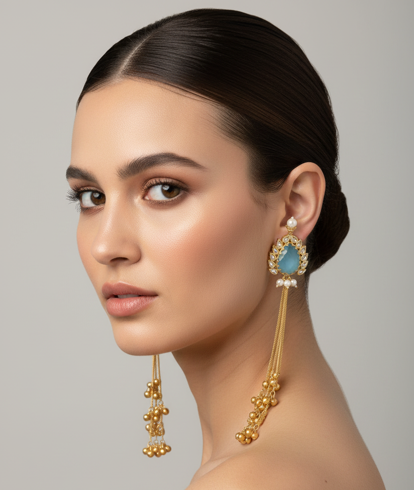 Woman wearing gold earrings with blue gemstones against a grey background