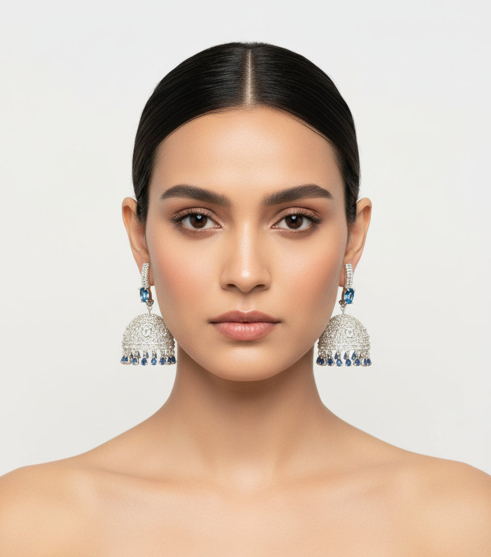 Woman wearing large silver earrings with blue stones on a plain background