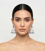 Woman wearing large silver earrings with blue stones on a plain background