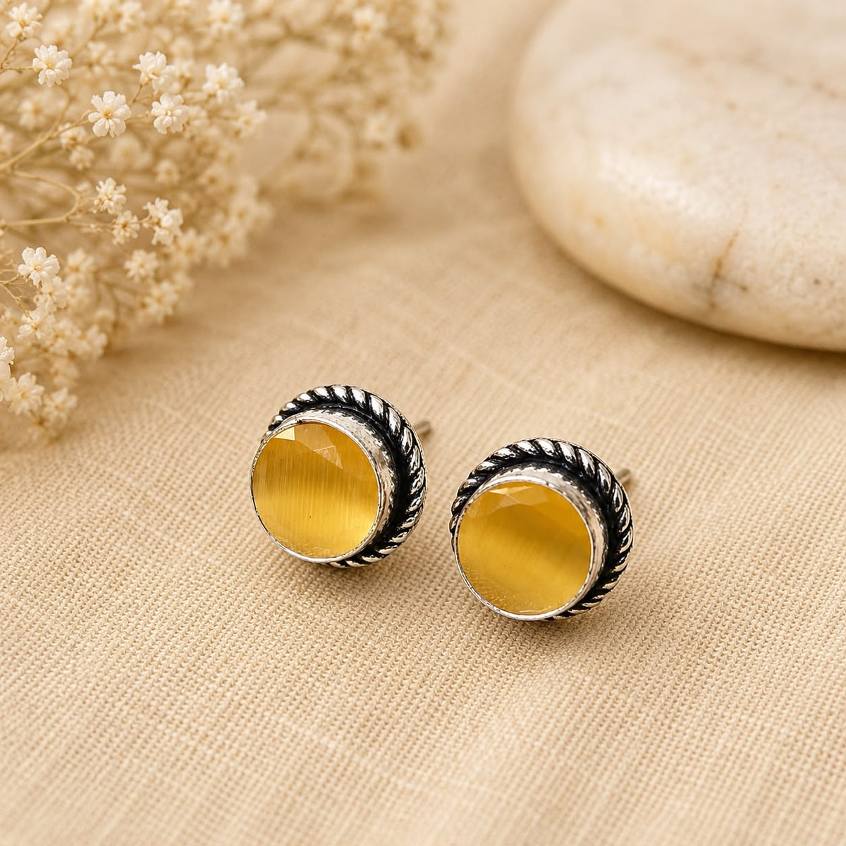 Round yellow earrings with silver detailing on a beige fabric background
