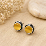Round yellow earrings with silver detailing on a beige fabric background