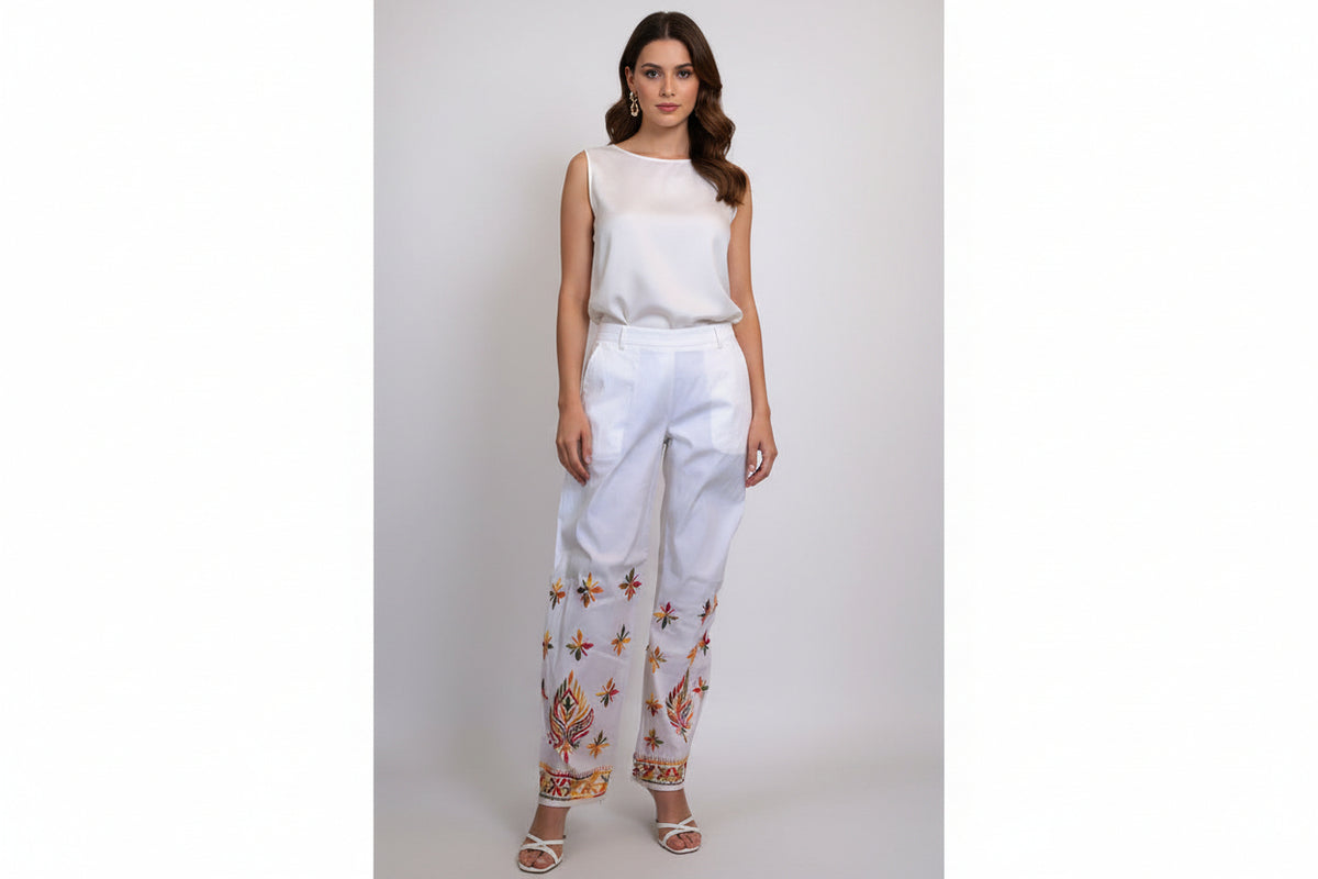 A pair of white stretchable cotton pants with pockets both sides and multi-coloured thread floral embroidery, featuring a relaxed fit with an adjustable drawstring waistband.