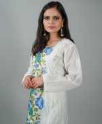 A woman modeling a long white cotton kurti with hand-painted floral Chikankari designs in blue, green, yellow, and pink.