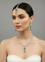 a rhodium-plated brass jewellery set with American diamond and emerald green central stone semi-precious stones, including a necklace, earrings, and maang tikka by famaza couture