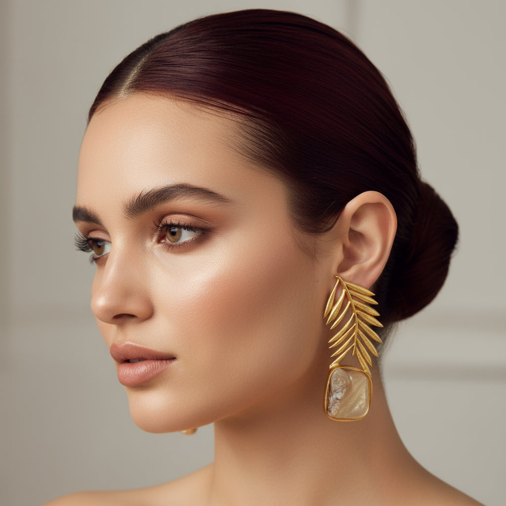 A pair of baroque mother of pearl earrings with golden feather accents, displayed on a wooden surface.