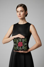 A black floral handcrafted tote bag with glass beads embroidered on a white silk base, displayed on a wooden surface with a greenery .background.
