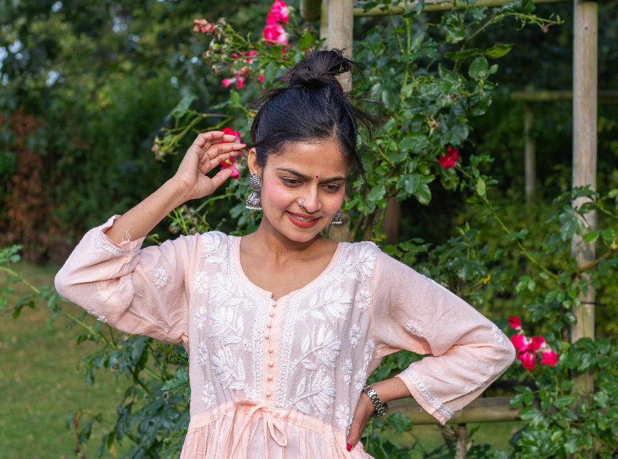 A woman standing outdoors wearing a short frock style kurti with embroidery and a tie-up waist, in a garden