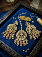 An ornate gold-toned traditional Indian jhumka necklace and matching earrings displayed on a deep blue velvet jewellery box. The jewellery features intricate filigree work, small clear stones, and clusters of pearl-like beads.