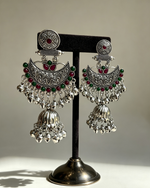 Pair of Deepika oxidised silver-tone Chandbali jhumka earrings with red and green accents on a black stand.