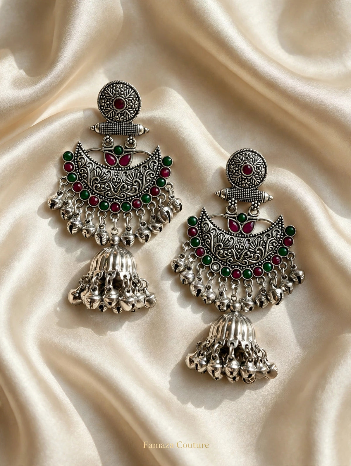 Pair of Deepika oxidised silver-tone Chandbali jhumka earrings with red and green accents on cream satin.