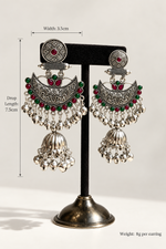 Deepika red and green silver-tone Chandbali jhumka earrings on a stand with size and weight labels.