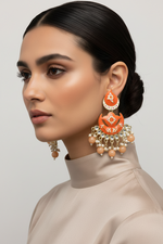 Woman wearing orange and gold earrings with a neutral background