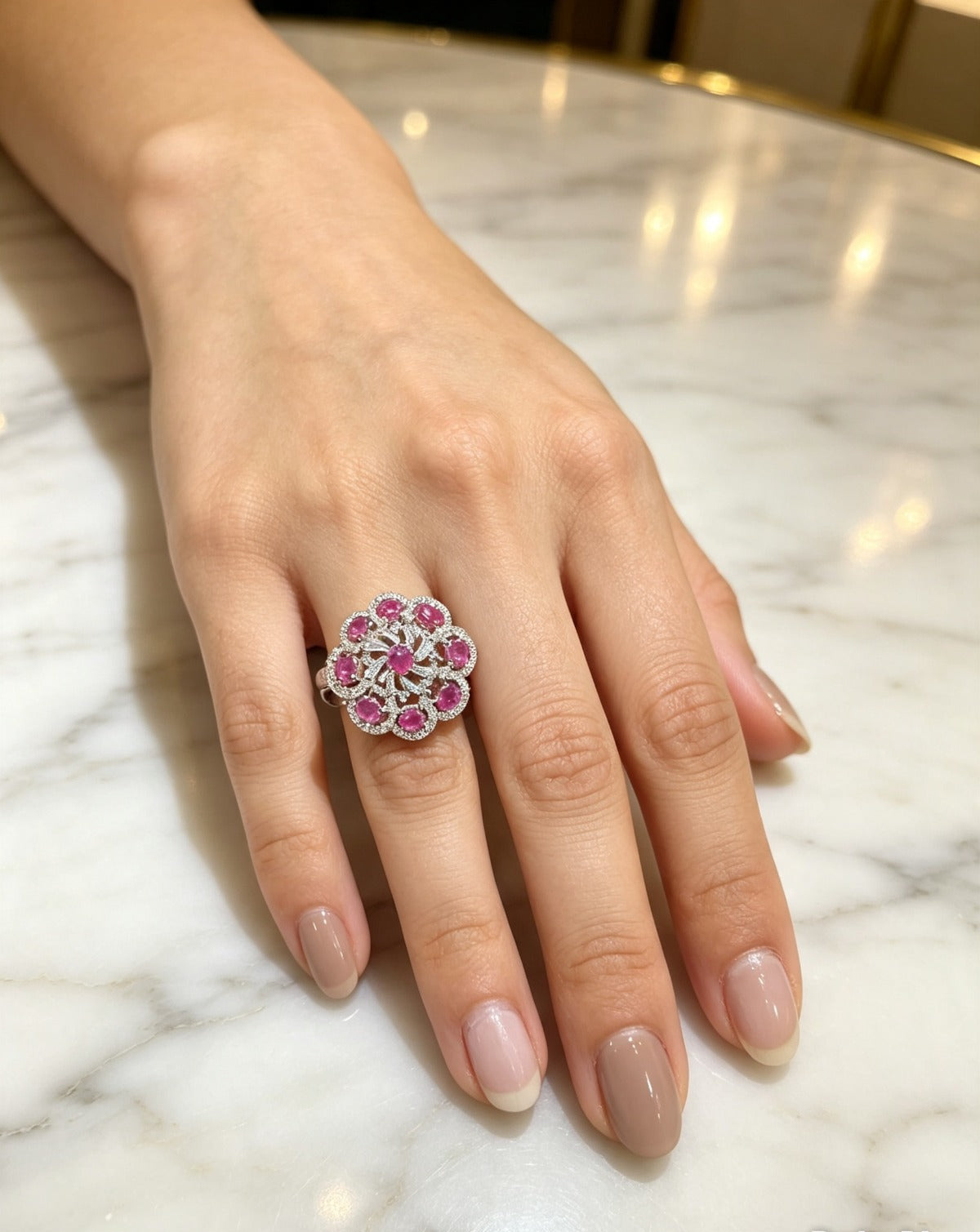 Close-up of a model wearing the Famaza Couture Royal Magenta-Pink Floral Cluster Statement Ring on a marble surface, showcasing its vibrant oval pink gemstones and silver-tone pavé crystal setting.
