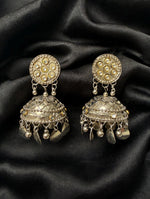 Pair of dual-tone kundan jhumka earrings on black fabric, showing round stone-set tops, floral dome detailing and dangling charms