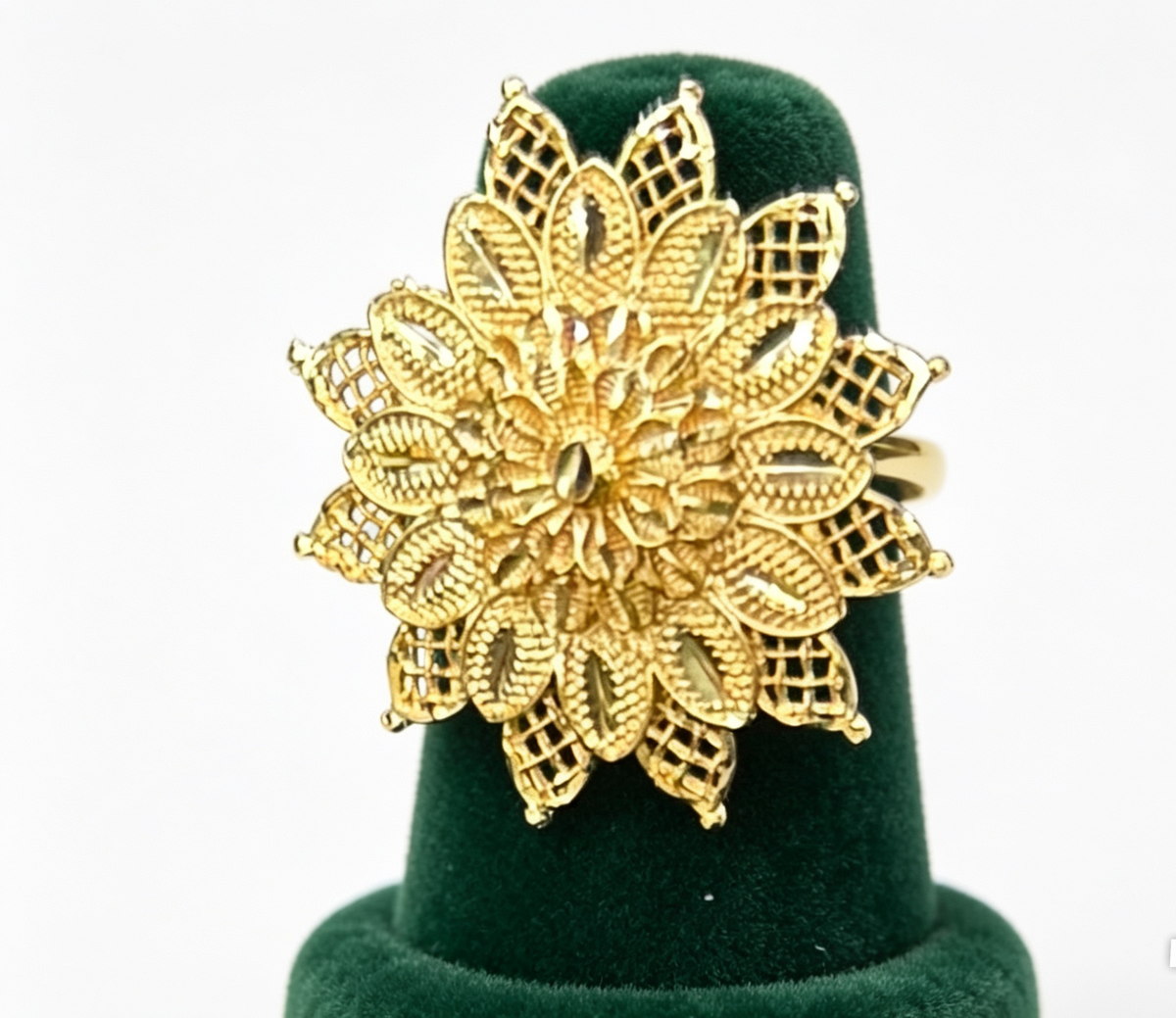 A large gold ring with an intricate, multi-layered filigree floral design, displayed on a dark green velvet ring cone against a white background.