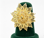 A large gold ring with an intricate, multi-layered filigree floral design, displayed on a dark green velvet ring cone against a white background.