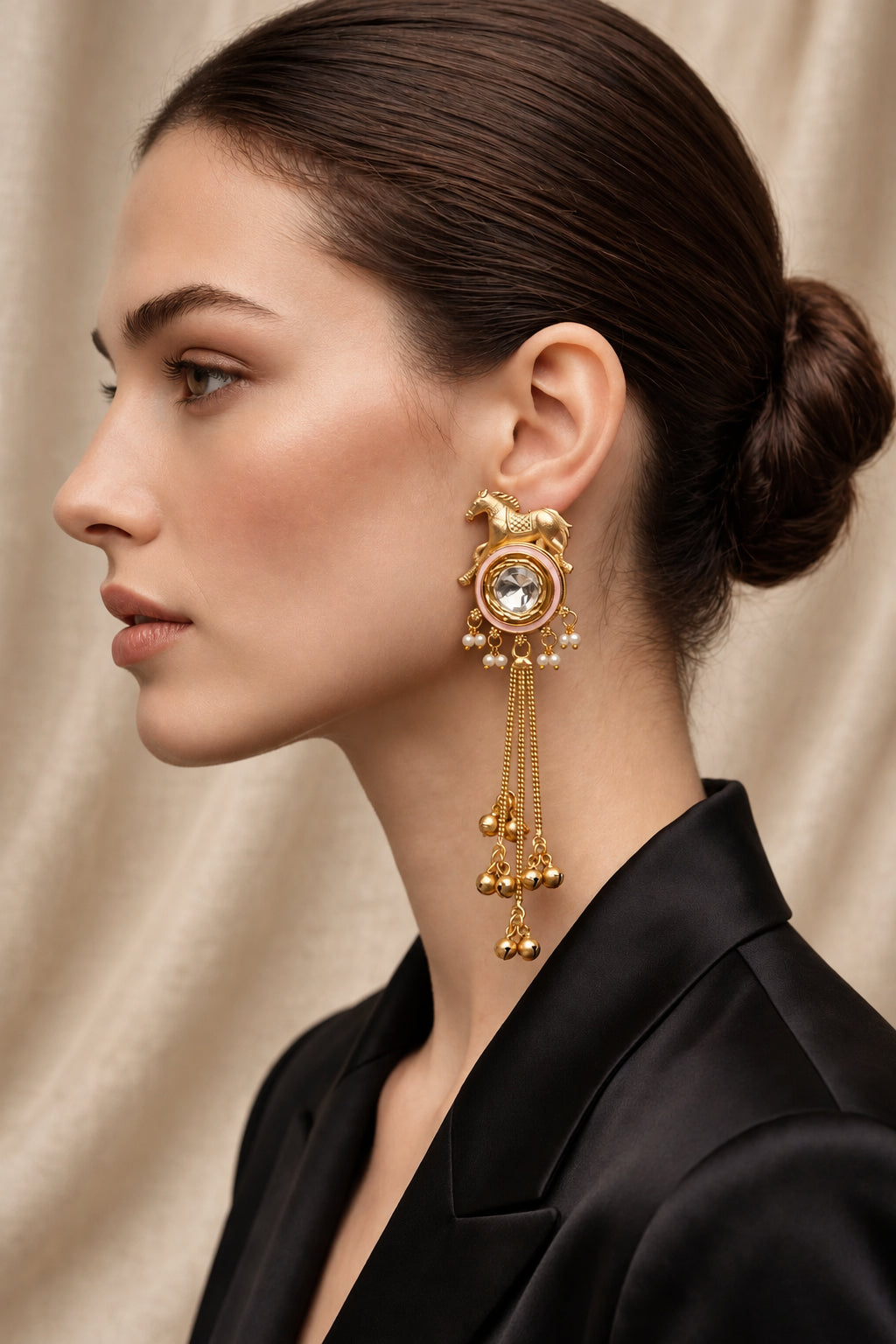 Model wearing a Golden Gallop horse motif earring with a reflective kundan centre and pink enamel pain in the outer circle, pearl-style accents and long gold-tone chain tassels.