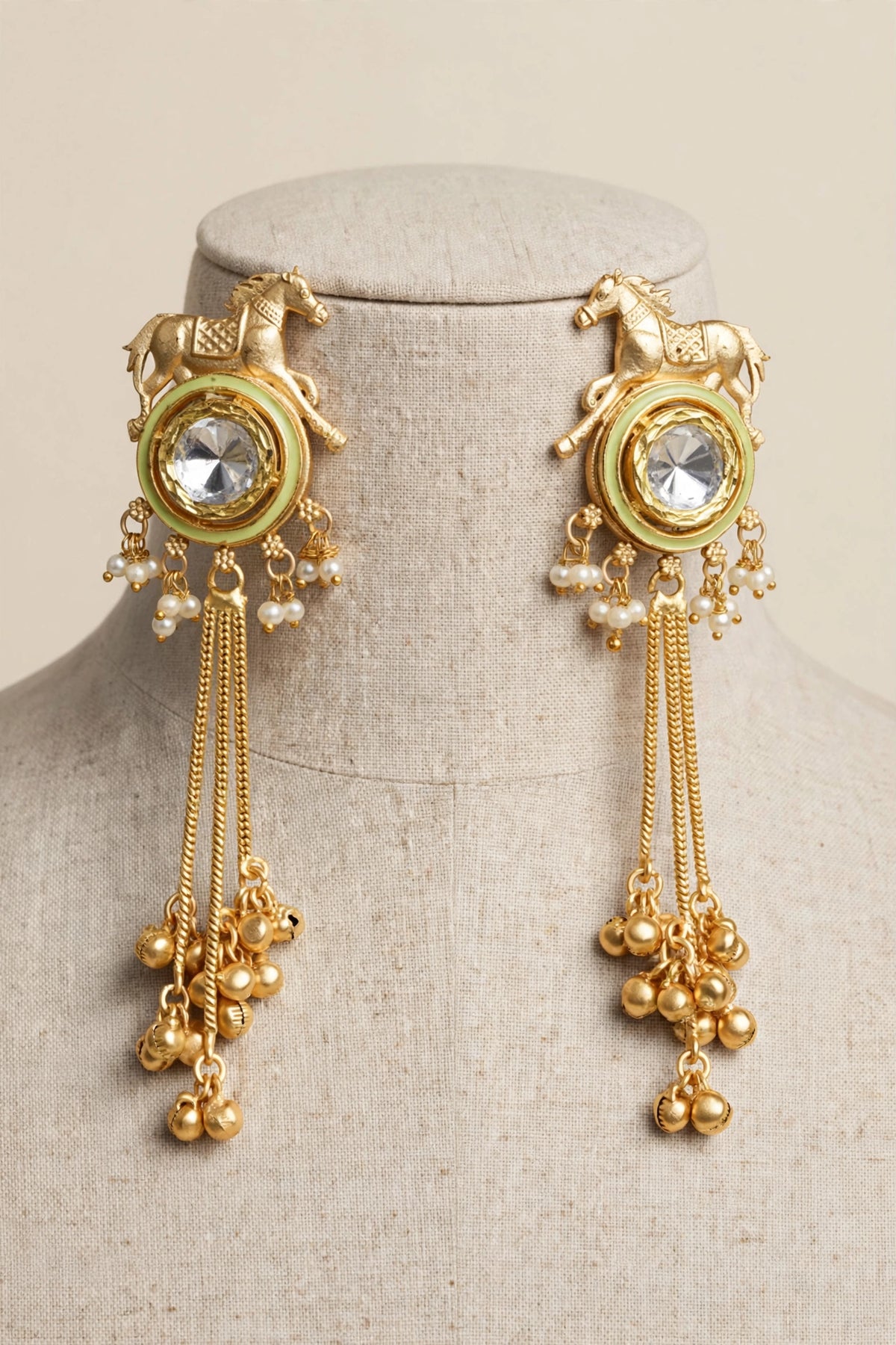 Lime Green Golden Gallop horse motif earrings with reflective kundan centres, pearl-style beads and gold-tone tassels on a linen bust