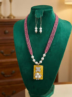 hot pink beaded necklace with a rectangular pendant and matching earrings on a green velvet stand.