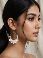 Ivory white shell-shaped dangle hoop earrings with faux pearls worn by a model.
