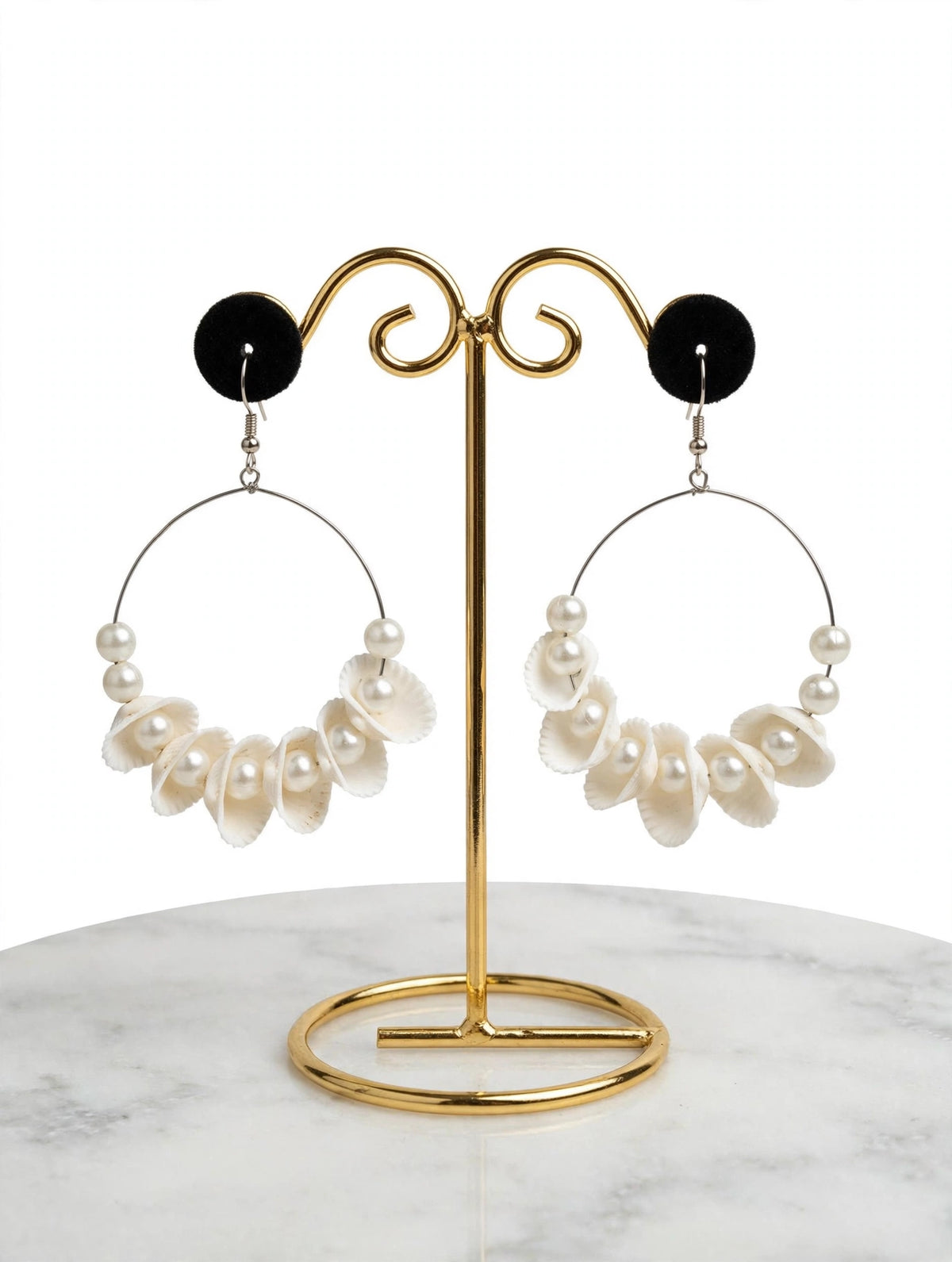 Ivory white shell-shaped dangle hoop earrings with faux pearls on a gold-tone display stand.