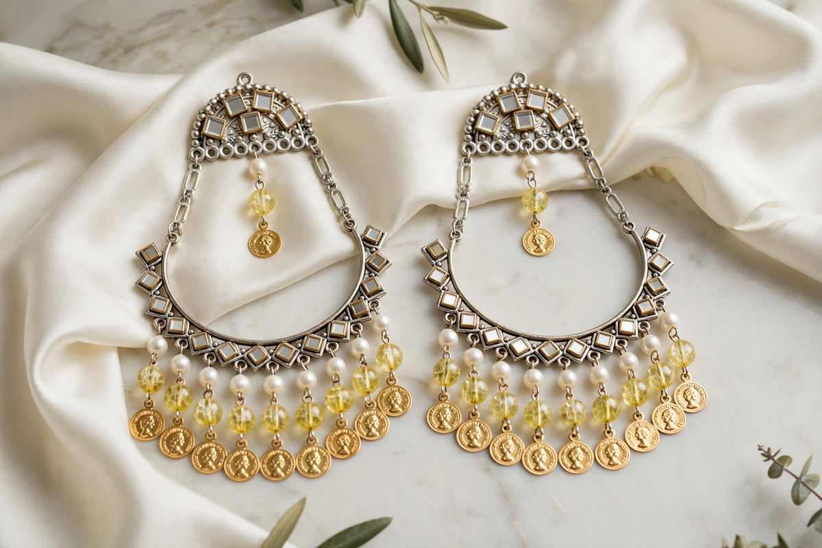 Pair of Kahani chandbali earrings with silver-tone crescent frames, yellow beads and gold-tone coin charms on ivory satin.