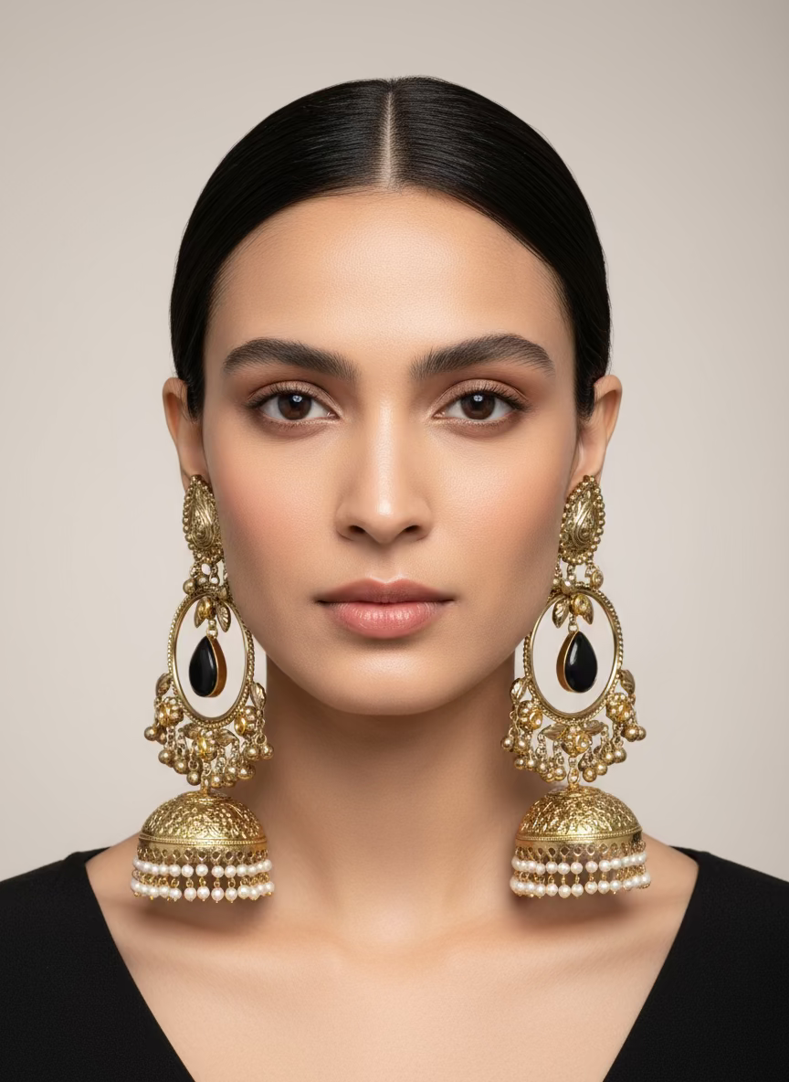 Gold and black stone earrings with dangling elements held by a hand, with a display of similar earrings in the background.