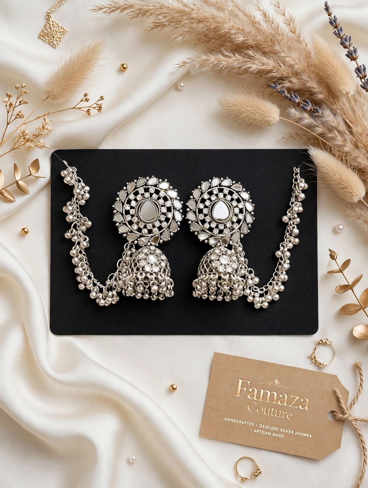 Silver-toned mirror-work Bahubali jhumka earrings with beaded Sahara ear chains on a black card over ivory satin.