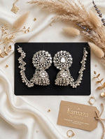 Silver-toned mirror-work Bahubali jhumka earrings with beaded Sahara ear chains on a black card over ivory satin.