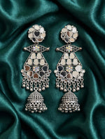 Mirror Muse silver-tone mirror jhumka earrings laid on green satin, with floral tops, iridescent crystal accents and ornate bell drops