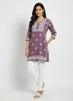model is wearing and posing in this Lilac colour short length Chikankari kurti with white floral hand embroidery with white jeans