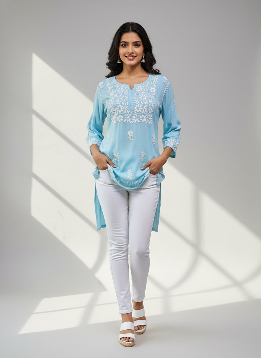 model is wearing and posing in this sky blue colour short length Chikankari kurti with white floral hand embroidery with white jeans